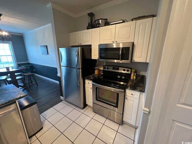 Kitchen with stainless steel appliances, ornamental molding, white cabinetry, light tile patterned flooring, and a chandelier