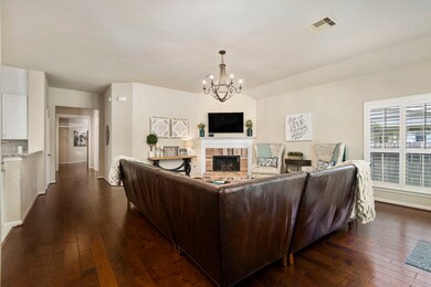 Spacious living room overlooks the wooded park in the back of the home, and features plantation shutters and a brick fireplace.