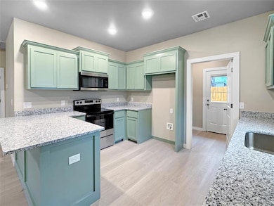 Kitchen area featuring mint cabinetry, granite countertops, modern lighting, and wood-style flooring. Note: Photos are of a similar home by the builder.