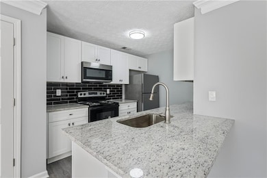 Kitchen with white cabinets, appliances with stainless steel finishes, backsplash, a textured ceiling, and light stone countertops