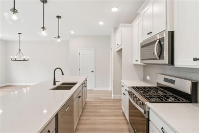 Kitchen with stainless steel appliances, a sink, a chandelier, baseboards, and light wood-type flooring