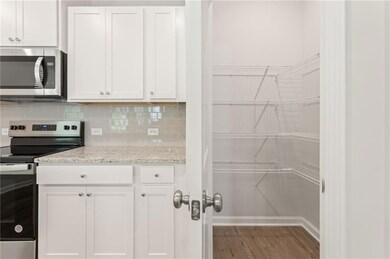 Kitchen featuring stainless steel appliances, tasteful backsplash, wood finished floors, and white cabinets