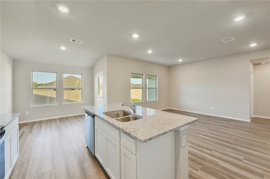 Kitchen with white cabinets, light wood-style floors, open floor plan, light stone countertops, and a center island with sink