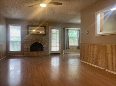 Unfurnished living room featuring a textured ceiling, wood finished floors, a ceiling fan, a wainscoted wall, and a fireplace
