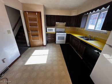 Kitchen with light countertops, dark brown cabinets, light flooring, backsplash, and white appliances