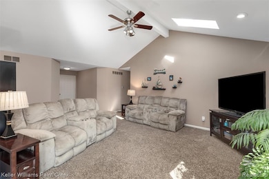 Carpeted living area with beam ceiling, ceiling fan, a skylight, and high vaulted ceiling