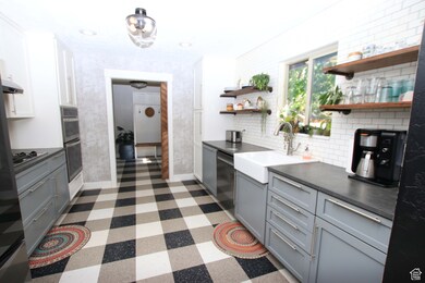 Kitchen with gray cabinetry, dark countertops, open shelves, appliances with stainless steel finishes, and tasteful backsplash