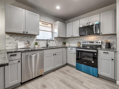 Kitchen with stainless steel appliances, light wood-type flooring, backsplash, dark stone counters, and recessed lighting