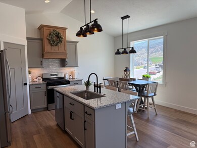 Kitchen featuring stainless steel appliances, gray cabinetry, backsplash, an island with sink, and a kitchen bar