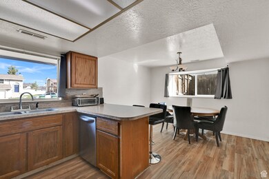 Kitchen with a textured ceiling, light wood-type flooring, brown cabinetry, decorative backsplash, and a peninsula
