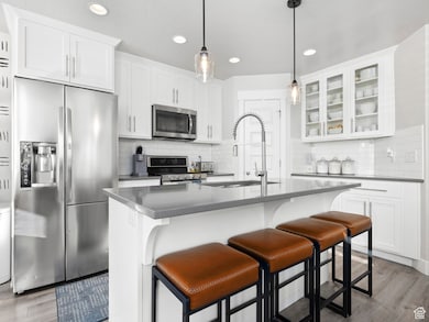 Kitchen featuring appliances with stainless steel finishes, dark wood-style floors, a breakfast bar area, white cabinetry, and glass insert cabinets