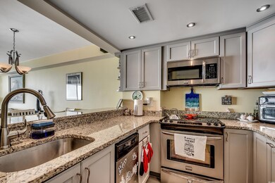 Kitchen with appliances with stainless steel finishes, a sink, gray cabinets, decorative light fixtures, and light stone counters