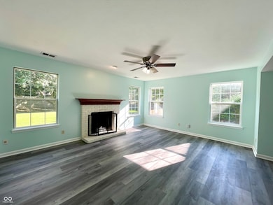 unfurnished living room with plenty of natural light, a brick fireplace, dark wood-type flooring, and a ceiling fan