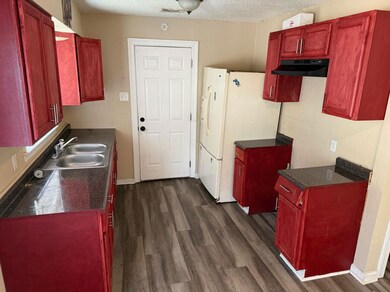Kitchen featuring reddish brown cabinets, under cabinet range hood, dark countertops, dark wood-style floors, and a textured ceiling