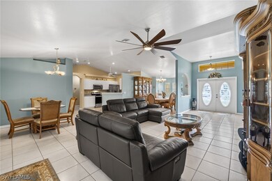 Living room with french doors, ceiling fan with notable chandelier, light tile patterned floors, and vaulted ceiling