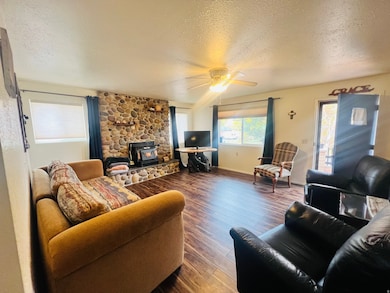 Living room featuring a wood stove, a textured ceiling, dark wood-style flooring, and ceiling fan