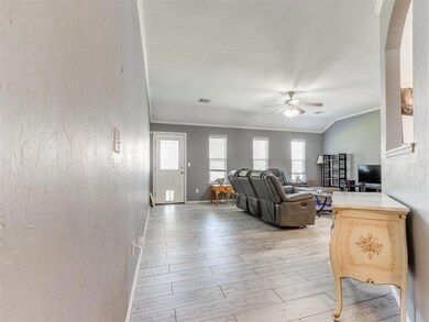 Living room featuring a ceiling fan, healthy amount of natural light, crown molding, arched walkways, and light wood-style floors
