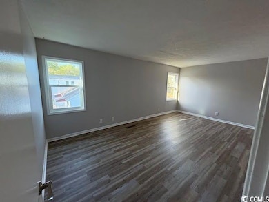 Empty room with dark wood-style flooring and baseb