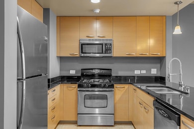 Kitchen featuring light brown cabinetry, dark ston
