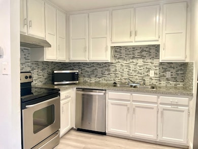 Kitchen with appliances with stainless steel finishes, white cabinetry, backsplash, and under cabinet range hood