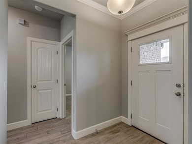Foyer entrance featuring light wood finished floors, crown molding, and baseboards