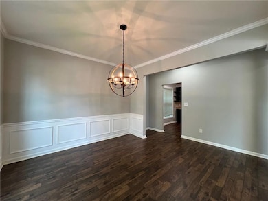 Empty room featuring a chandelier, dark wood finished floors, crown molding, and wainscoting