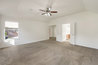 Spacious, bright primary bedroom with neutral carpet, a ceiling fan, and a large windows offering natural light. The room connects to an en-suite bathroom through double doors and has a private sitting room