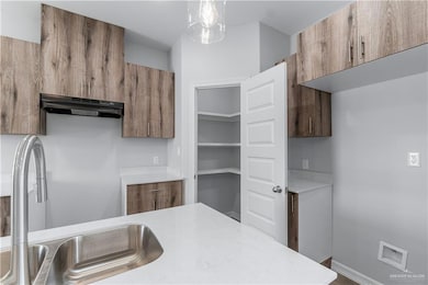 Kitchen with under cabinet range hood, light countertops, a sink, and brown cabinetry