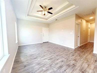 Unfurnished room with light wood finished floors, a raised ceiling, and a ceiling fan