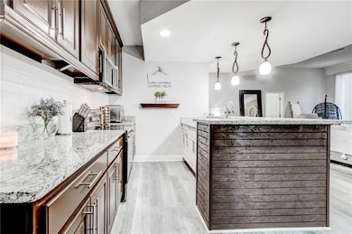 Downstairs kitchen with stainless steel electric stove, dark brown cabinetry, pendant lighting, and light wood-type flooring