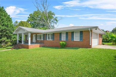 Ranch-style home featuring brick siding, covered porch, driveway, a front lawn, and an attached garage