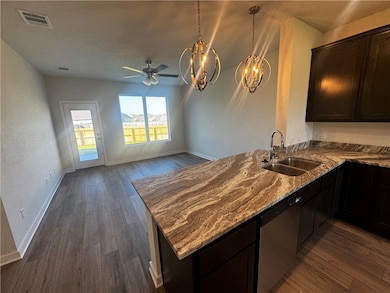 Kitchen with dark stone countertops, a peninsula, dark wood-type flooring, stainless steel dishwasher, and a chandelier