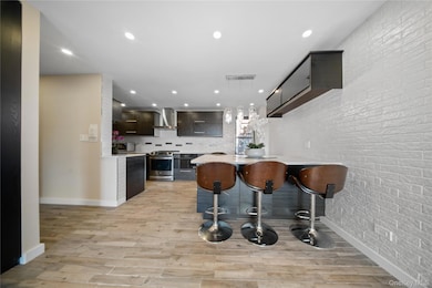 Kitchen featuring modern cabinets, a breakfast bar area, brick wall, light wood-style flooring, and pendant lighting