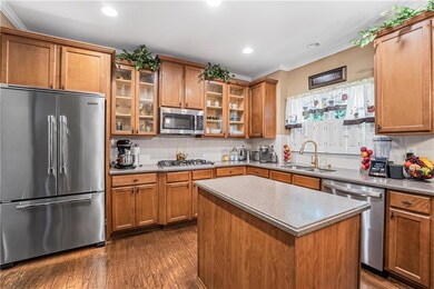 Kitchen with stainless steel appliances, crown molding, brown cabinets, dark wood-type flooring, and recessed lighting