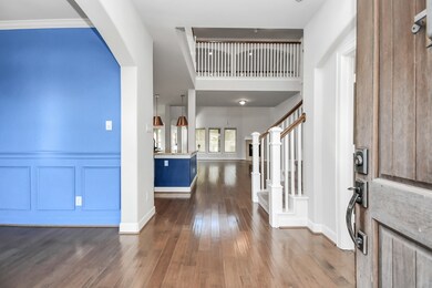 This photo showcases a spacious interior with an open floor plan, featuring hardwood floors, elegant white trim. The view includes a glimpse of a modern kitchen and an upstairs balcony, offering a blend of stylish design and comfortable living space.