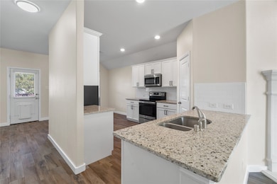 Kitchen with white cabinets, backsplash, stainless steel appliances, light stone countertops, and dark wood-type flooring