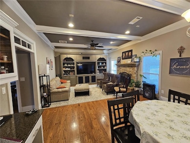 Dining room featuring ceiling fan, wood finished floors, beamed ceiling, crown molding, and a stone fireplace