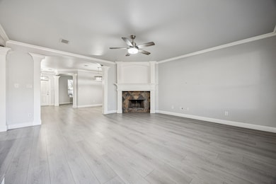 Unfurnished living room featuring ornamental molding, ceiling fan, a tile fireplace, light wood-type flooring, and ornate columns