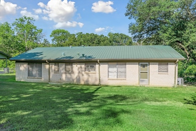 Rear view of house with a metal roof, brick siding, a lawn, and view of scattered trees