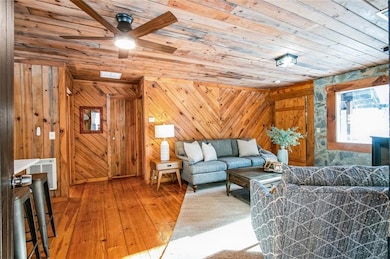 Living room featuring wooden ceiling, hardwood / wood-style floors, wooden walls, and ceiling fan