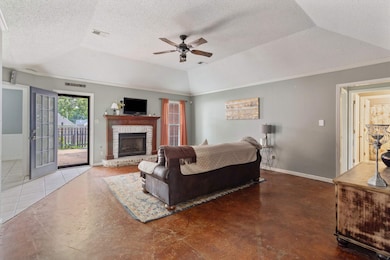 Living area featuring a ceiling fan, baseboards, a brick fireplace, a tray ceiling, and a textured ceiling