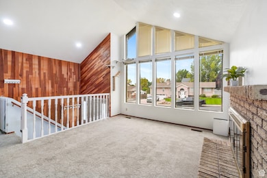 Unfurnished room featuring wood walls, carpet, high vaulted ceiling, and a residential view