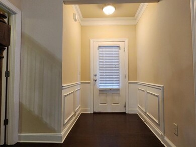 Doorway featuring crown molding, dark wood-style flooring, wainscoting, and a decorative wall