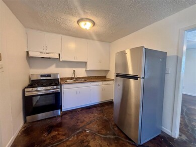 Kitchen with stainless steel appliances, white cabinetry, a textured ceiling, under cabinet range hood, and unfinished concrete floors