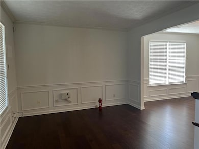 Spare room featuring a decorative wall, dark wood finished floors, a wainscoted wall, and ornamental molding