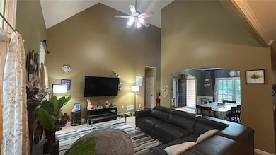 Carpeted living room with arched walkways, high vaulted ceiling, a ceiling fan, and baseboards
