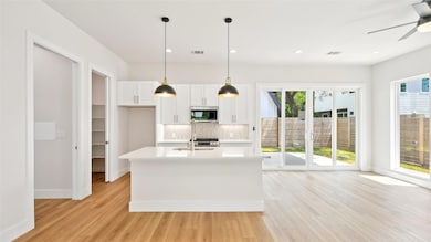 Kitchen with backsplash, white cabinetry, decorative light fixtures, light wood-style flooring, and a kitchen island with sink
