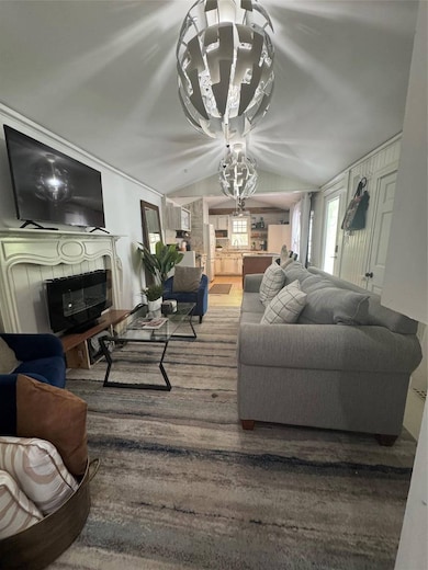 Living room with a tiled fireplace, lofted ceiling, a chandelier, and wood finished floors