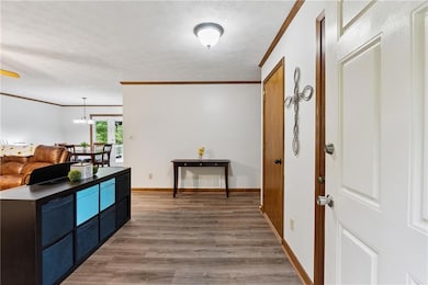 Hall with crown molding, light wood-style flooring, baseboards, a textured ceiling, and a chandelier