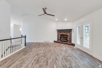 Unfurnished living room with vaulted ceiling, light wood-style floors, french doors, a glass covered fireplace, and a ceiling fan